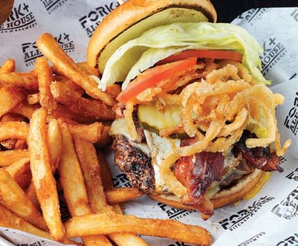 A cheeseburger topped with everything sits in a basket surrounded by fries.