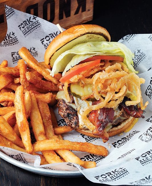 A cheeseburger topped with everything sits in a basket surrounded by fries.