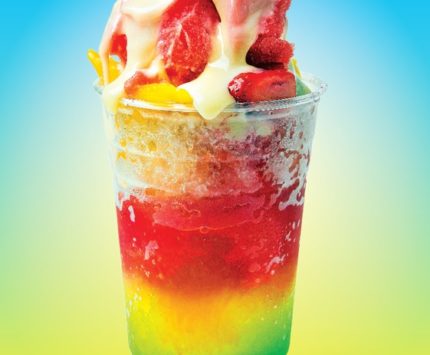 A shaved ice treat in a rainbow of colors, topped with fruit.