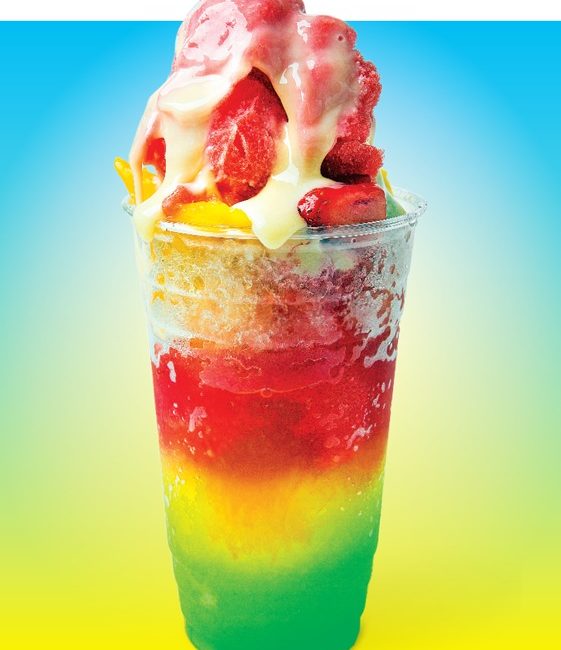 A shaved ice treat in a rainbow of colors, topped with fruit.