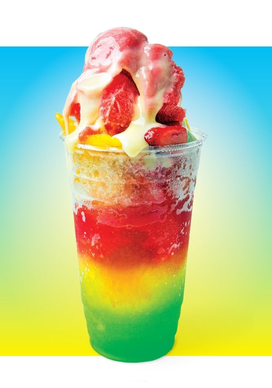 A shaved ice treat in a rainbow of colors, topped with fruit.