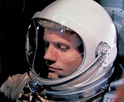 A man sits with a space helmet and suit on.