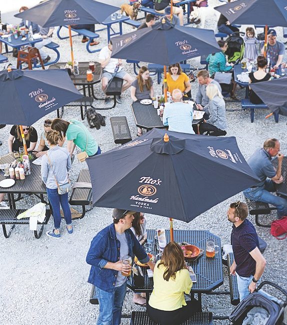 An outdoor patio with picnic tables and swarms of people and dogs.