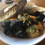 A bowl of seafood and veggies with grilled slices of bread