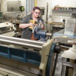 A woman stands inside a workshop while operating a machine.