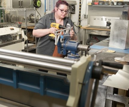 A woman stands inside a workshop while operating a machine.