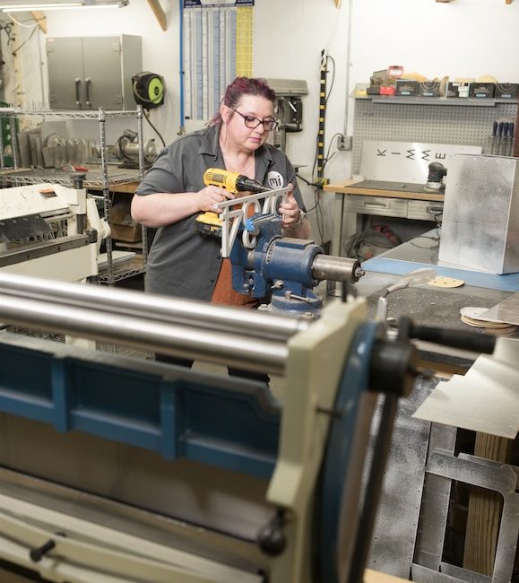 A woman stands inside a workshop while operating a machine.