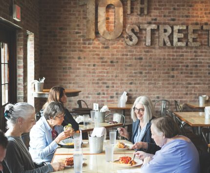 Women sit inside a restaurant adorned with brick walls and enjoy a meal.