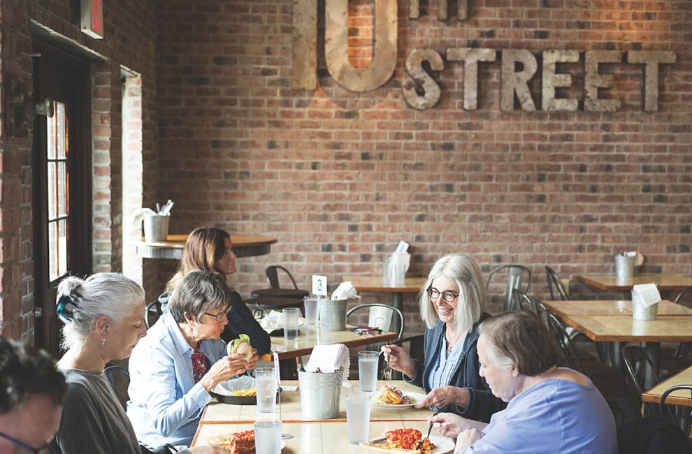 Women sit inside a restaurant adorned with brick walls and enjoy a meal.