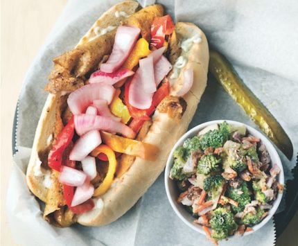 A vegan sandwich packed with veggies sits alonsie a broccoli salad.