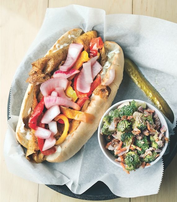 A vegan sandwich packed with veggies sits alonsie a broccoli salad.