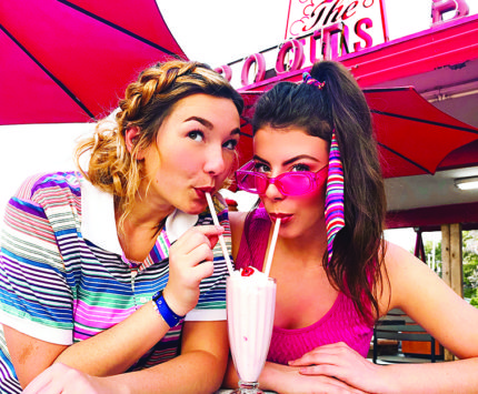 Two women share a milkshake at a classic diner.