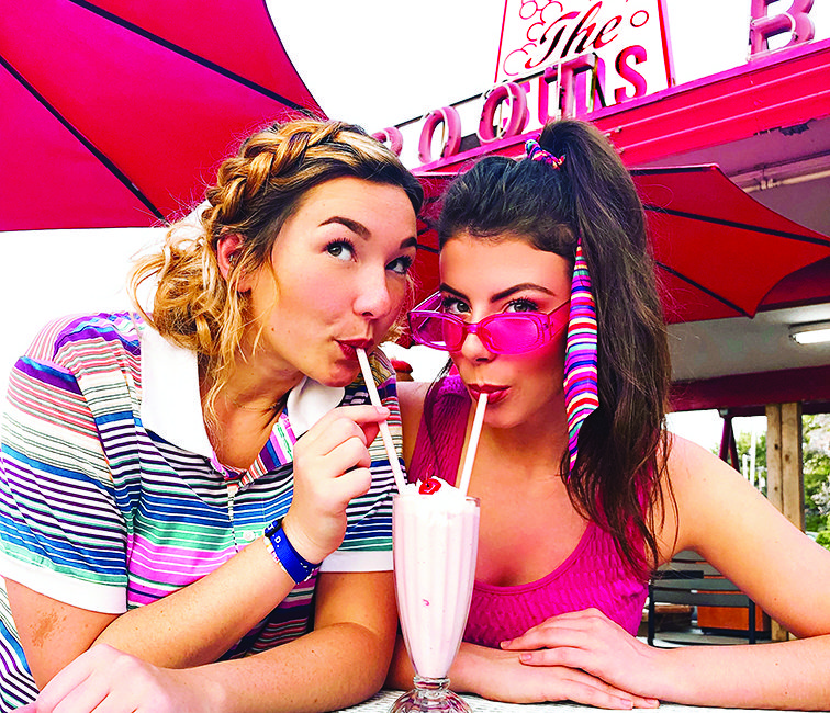 Two women share a milkshake at a classic diner.