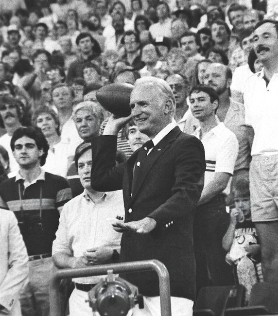 Historic black and white photo of a man throwing a football from the stands to begin an NFL game.