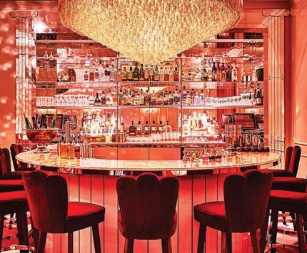 A stylish bar decked out with pink light and a massive chandelier.