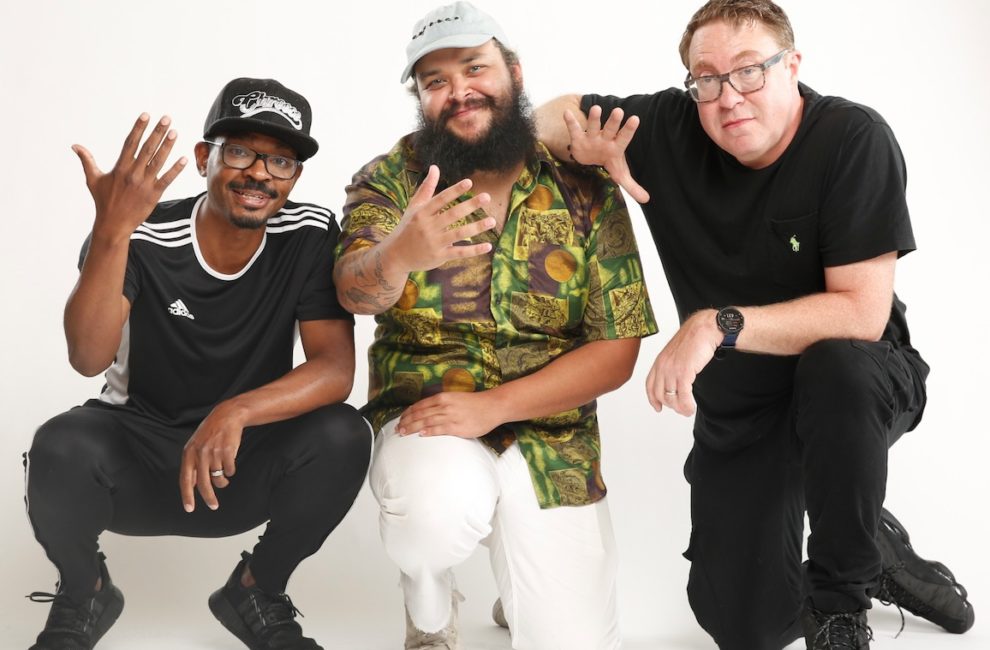 Three guys stand against a white background.