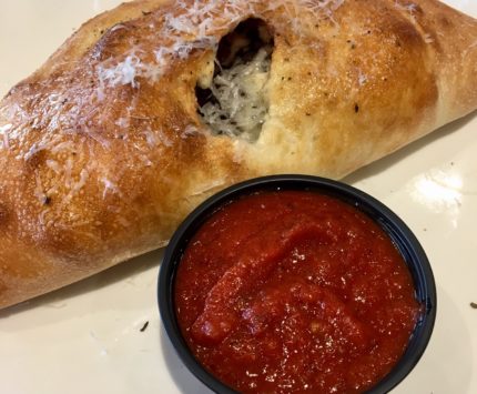 A golden brown calzone on a white plate with red marinara sauce.