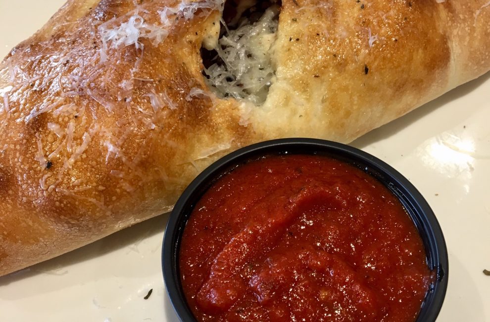 A golden brown calzone on a white plate with red marinara sauce.