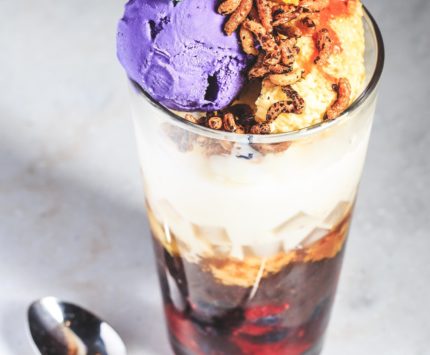 A large drinking glass filled with ice cream, marshmallow, strawberries, and other toppings.