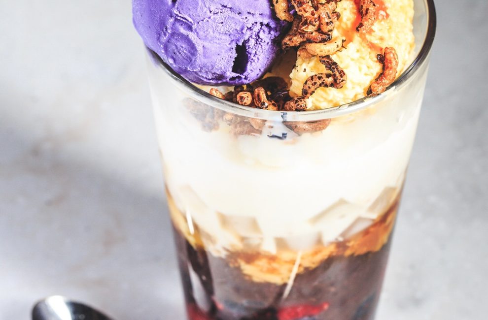 A large drinking glass filled with ice cream, marshmallow, strawberries, and other toppings.