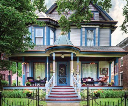 The exterior of a Victorian-era home that is painted in blues, purples, and reds.