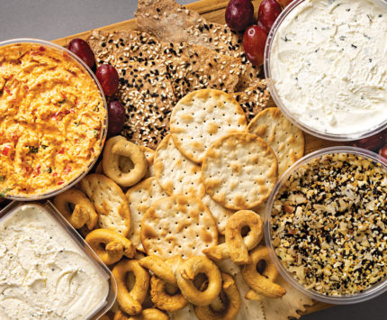 a board with cheeses, crackers, pretzels, and grapes