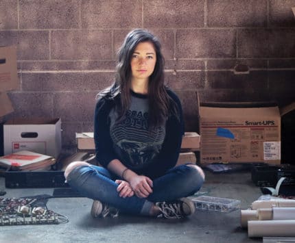 A woman sitting with boxes and machine parts