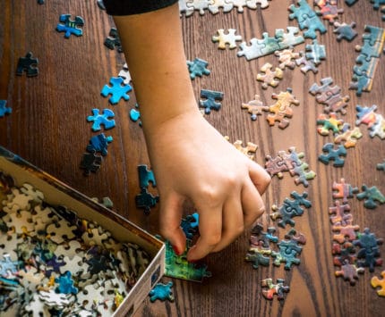 A youth's hand collects and assembles puzzle pieces of a jigsaw on a wooden background. background selective blur, concept