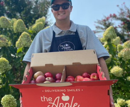 Man holding a red box containing apples