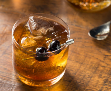 and old fashioned cocktail with two cherries on a metal pick