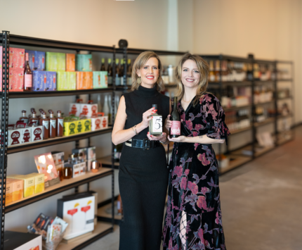Loren's AF owners and sister pose in front of shelves of nonalcoholic beverages like the bottles they hold