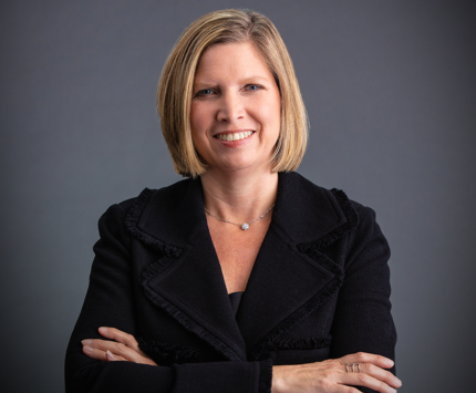 Jennifer Rumsey, Cummins CEO sports a blonde bob and a black jacket in this photo studio image with a grey background
