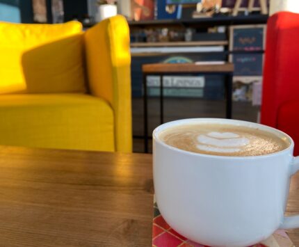 a white mug of coffee with a yellow chair and red chair in background
